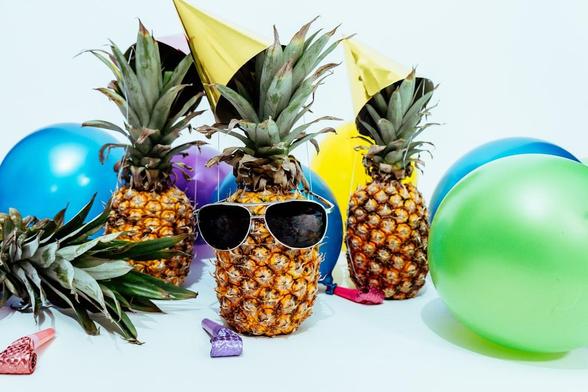 Ein mit mehreren Ananas nachgestelltes Geburtstagsfoto. Es sind Partyhüte, Luftballons und mehr Dekoration auf dem Bild verteilt.